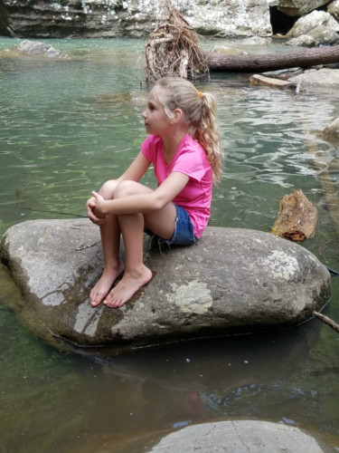 A Father's perspective. Daughter sitting on a rock in a river.