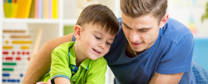 Father and son read together sitting on the floor. Kid boy reading story book with his dad at home.