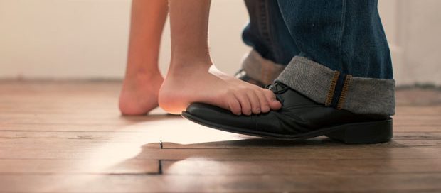 Stutter-Step Shuffle Image of child's bare feet standing on father's shoes.